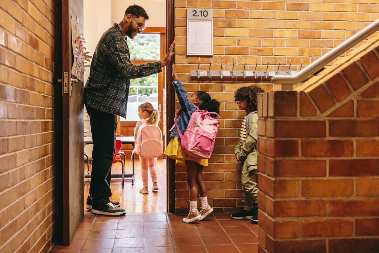 Kindergarten teacher greeting his students at the door to the classroom with a high five