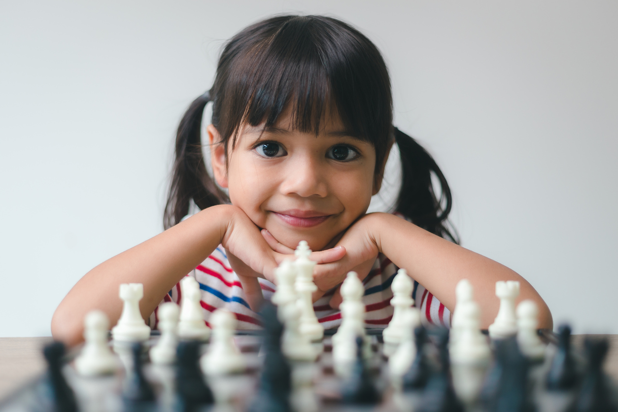A young child looking across a chessboard at you with a smile