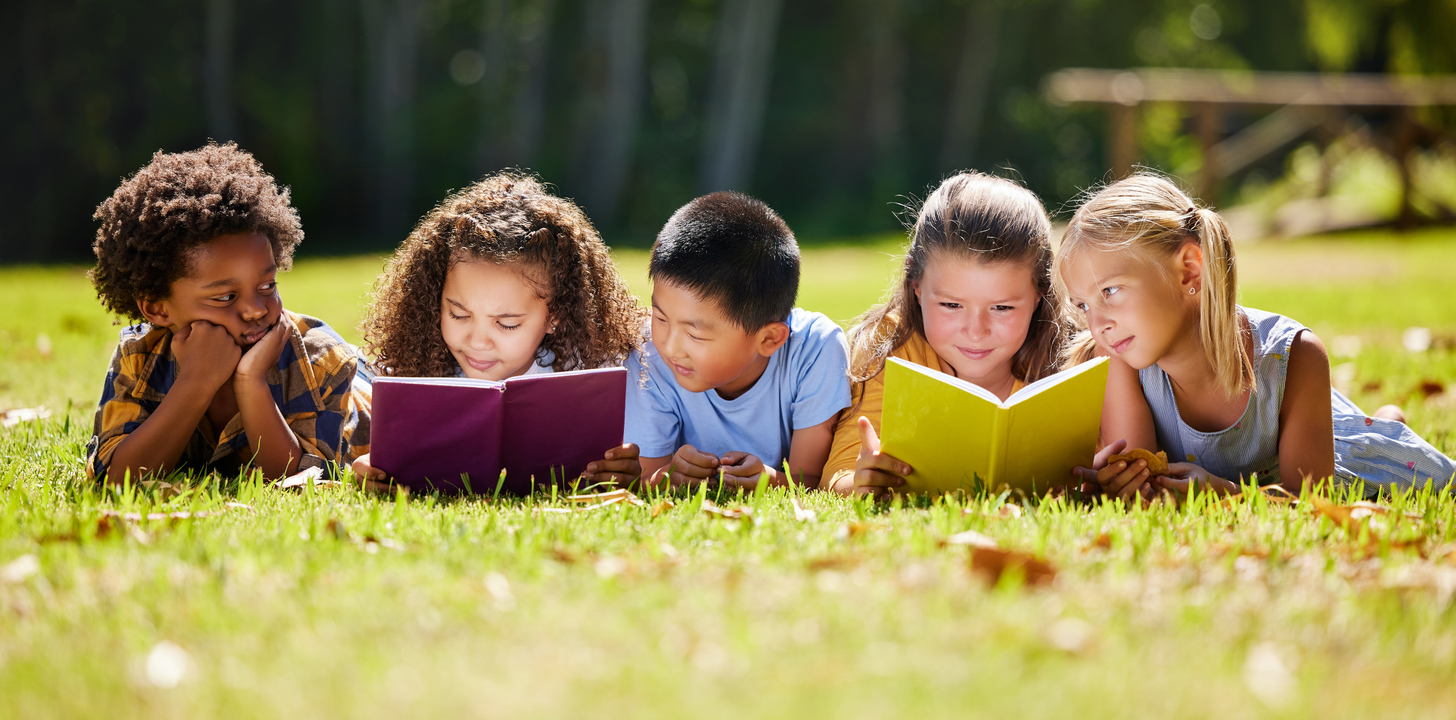 Five children reading books in the grass outside together