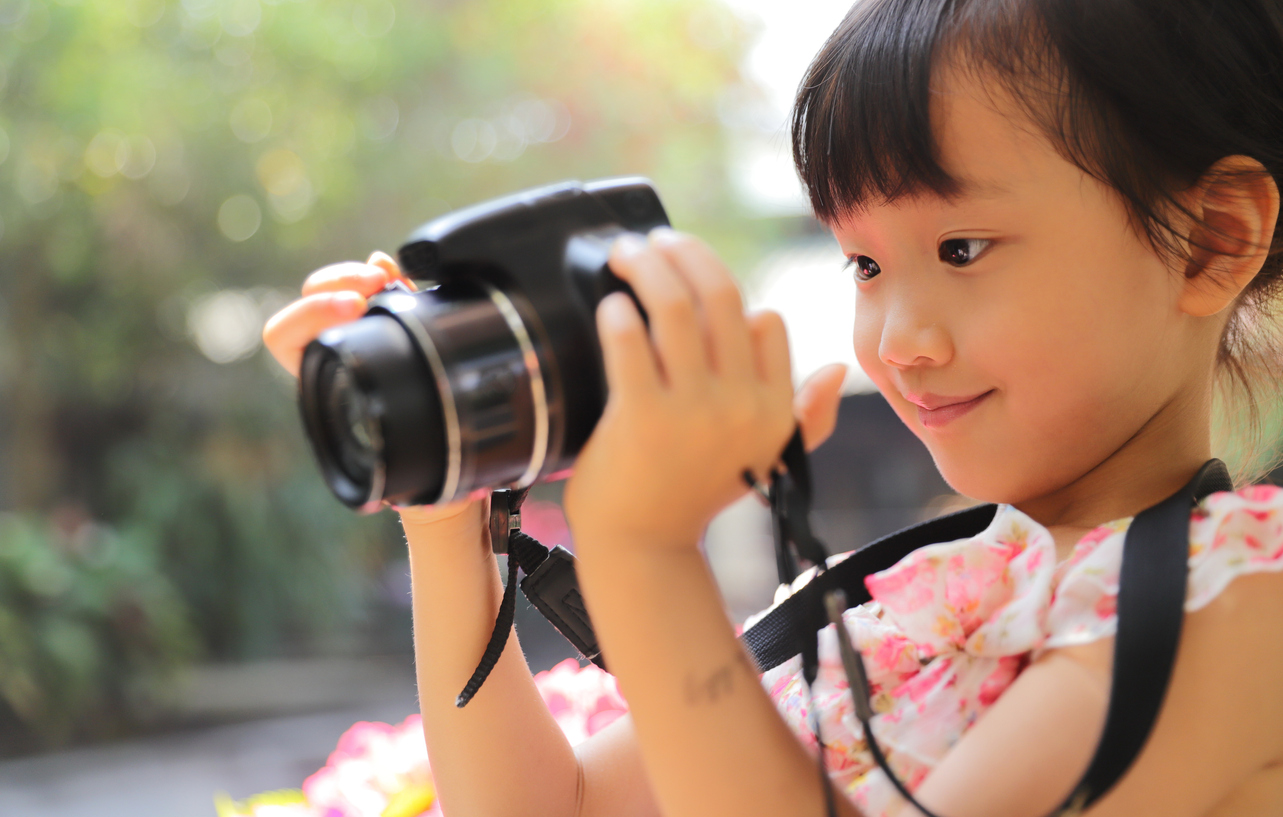 A young child holding up a camera and looking at the digital display with a smile